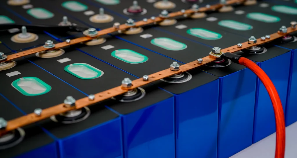 Industrial LiFePO4 battery module array with blue/black ABS casings featuring green polycarbonate inspection windows, interconnected by gold-plated copper busbars secured with hexagonal nuts. Red power cables extend from terminal ends demonstrating parallel circuit configuration for scalable energy systems.